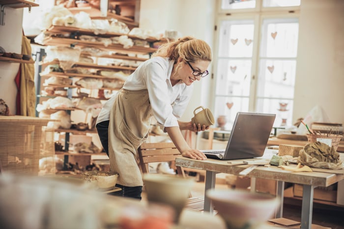 Potter using laptop in pottery shop.