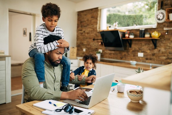 A child sitting on the shoulders of an employee working at home.