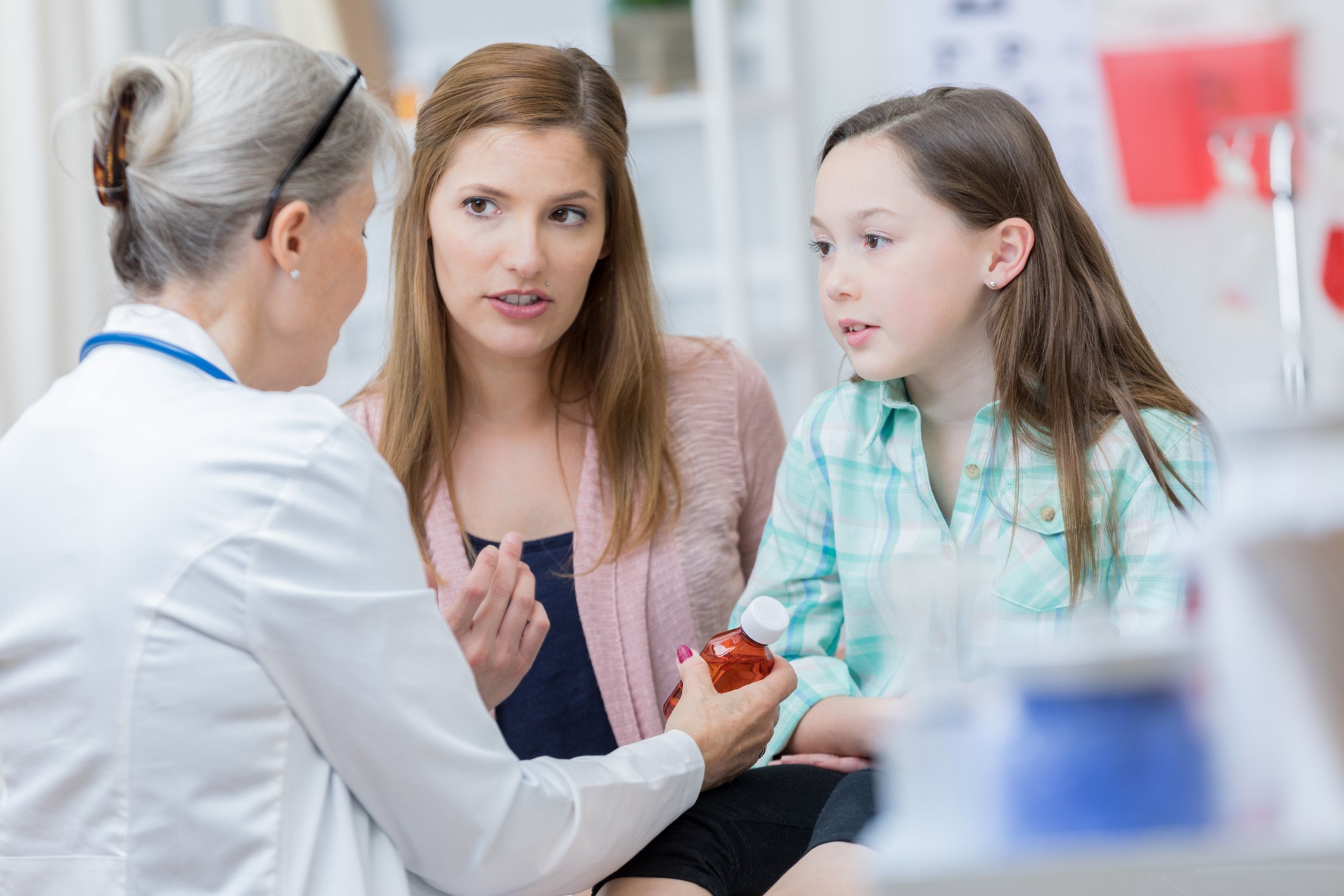 A pharmacist hands a bottle to two customers.