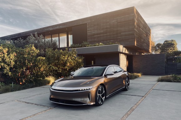 gold Lucid Air in driveway of modern home.