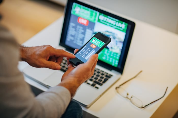 A person betting on a game with their phone and laptop.