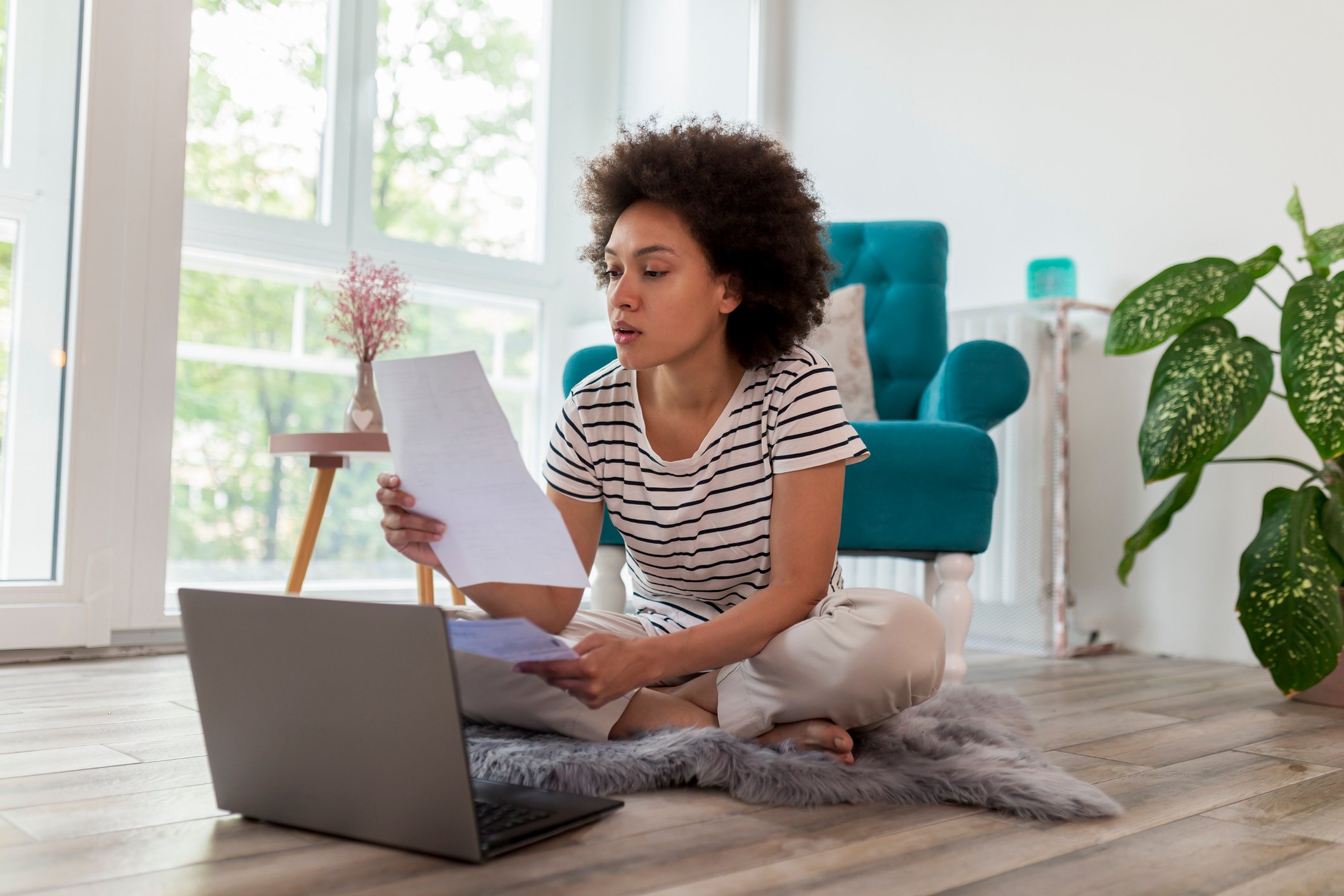 An investor sits on the floor in a living room and works on a laptop.