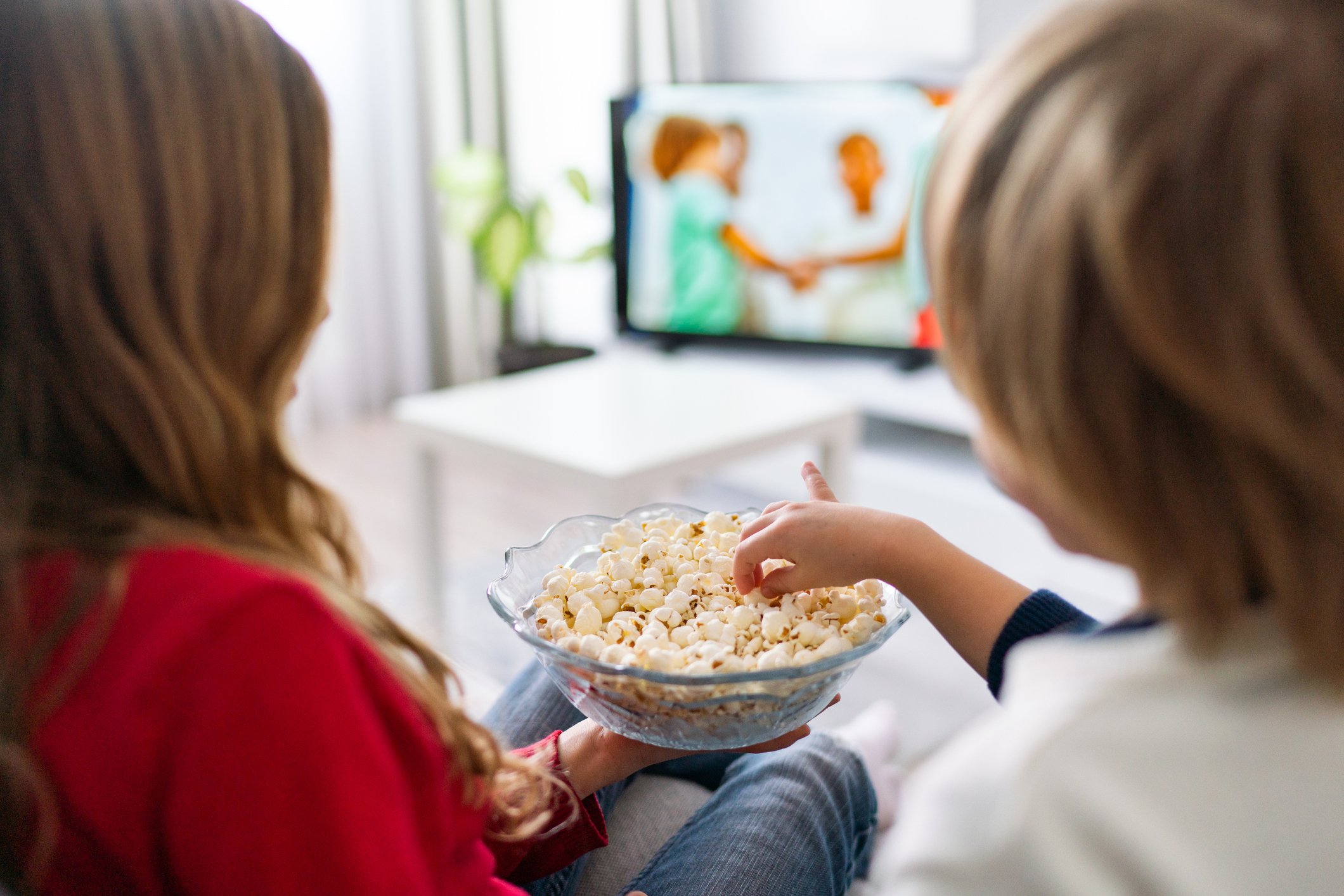 Two people eating popcorn and watching television.