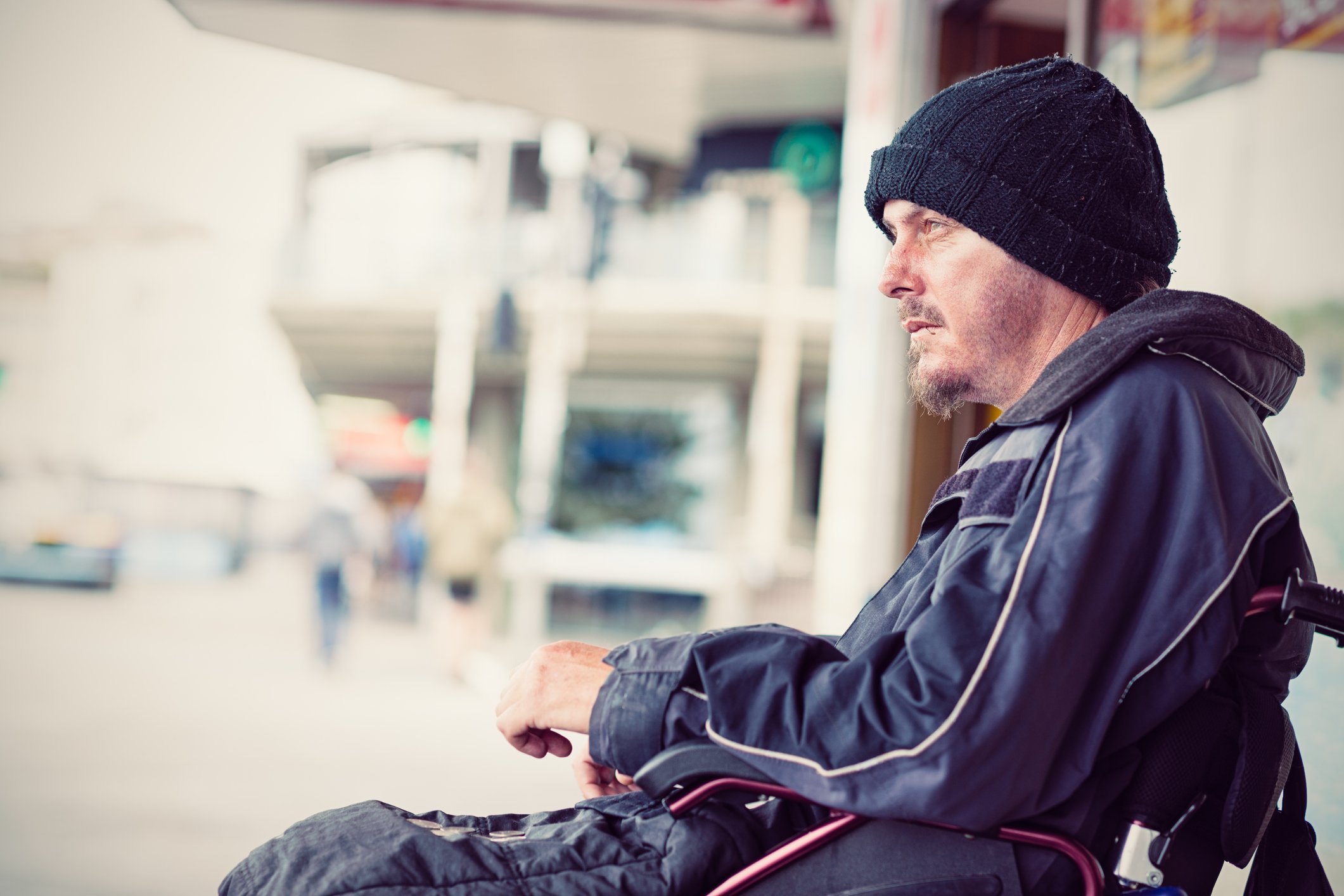 A person in a wheelchair, sitting outside wearing a hat and jacket. 