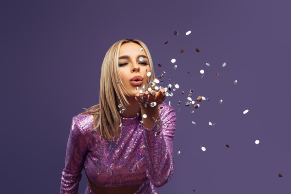 A woman in a purple dress blowing glittery objects