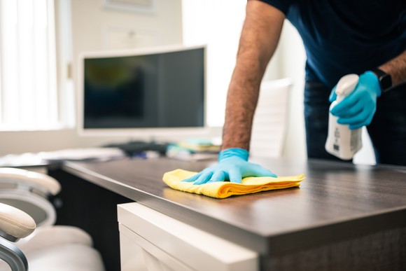 A person sanitizes an office desk.