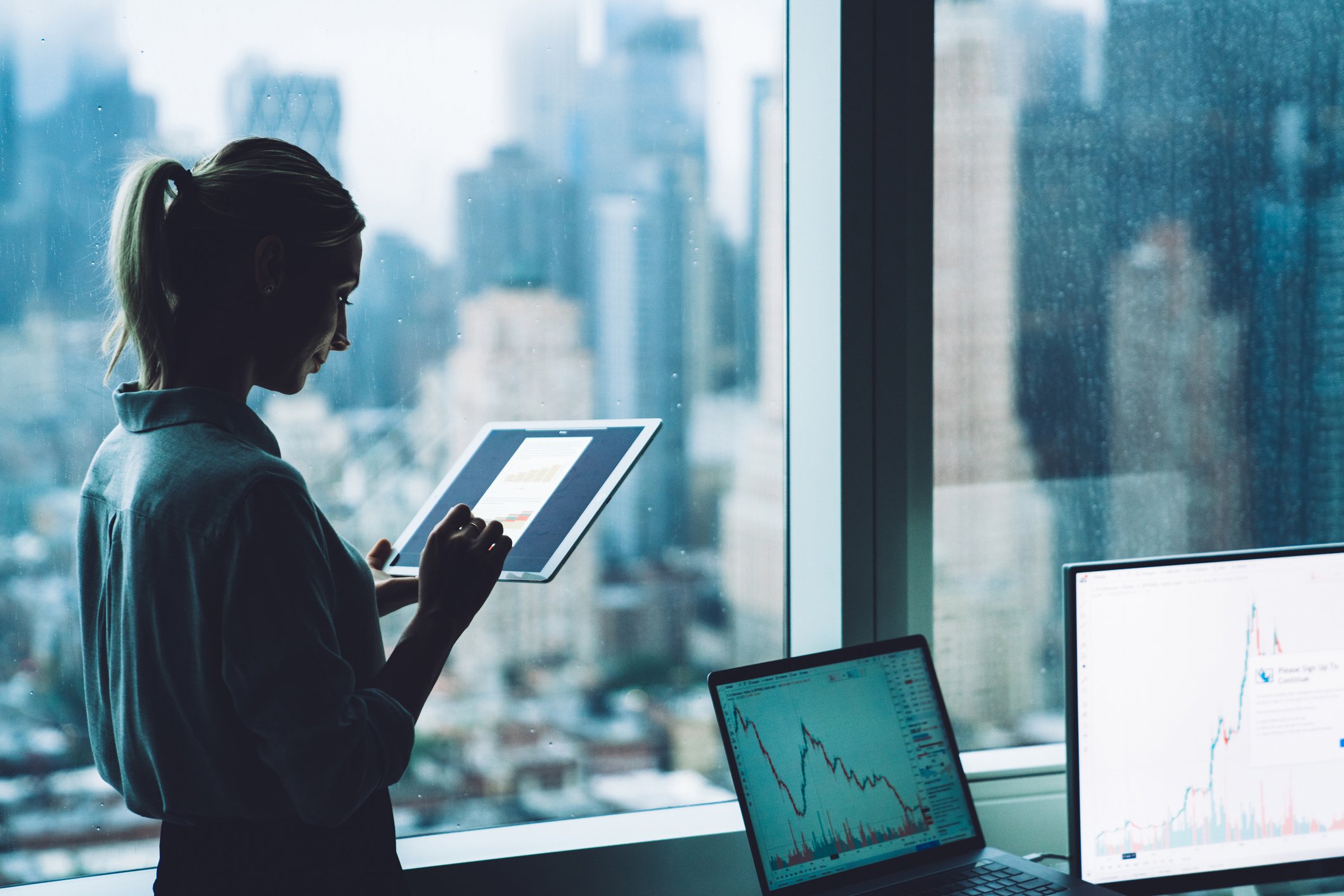 A person standing in front of an office window, using a tablet.