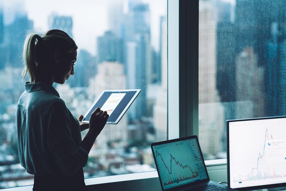 A person standing in front of an office window, using a tablet.