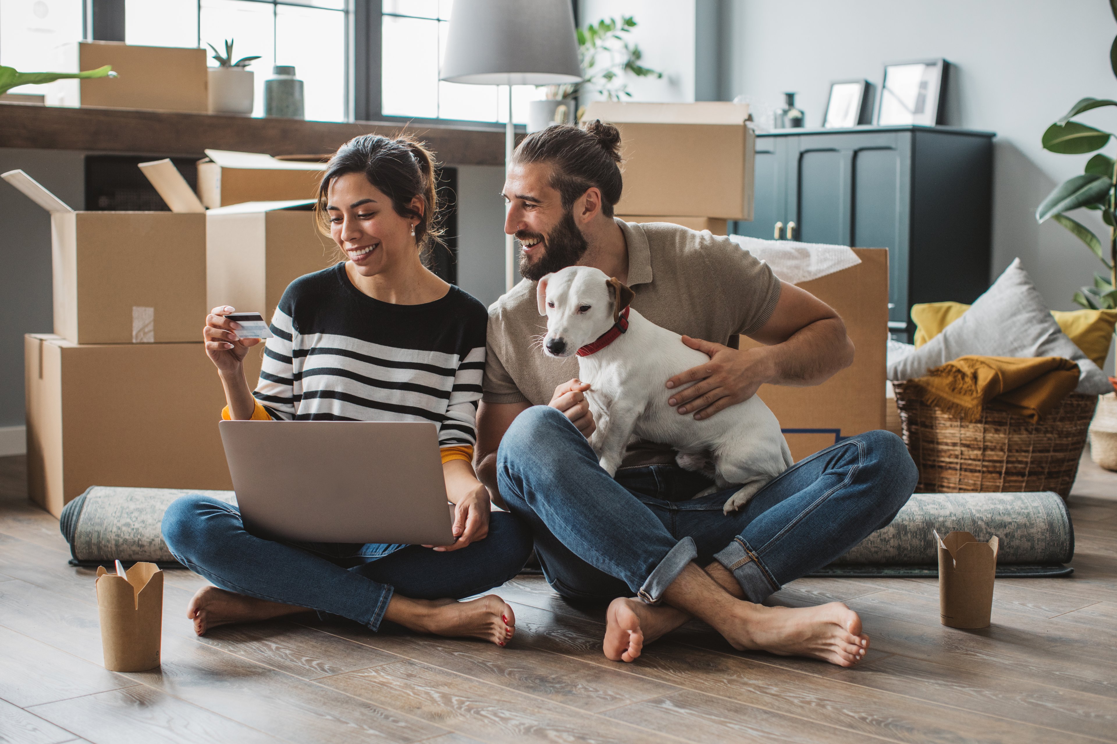 Two adults and dog sitting in a room with packing boxes.