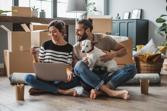 Two adults and dog sitting in a room with packing boxes.