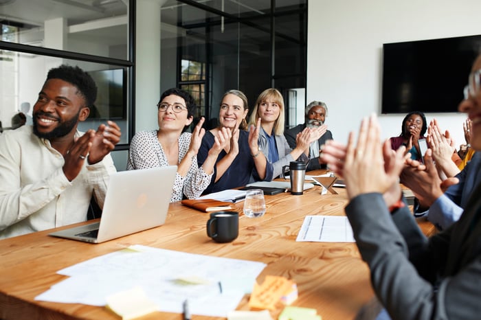 People in conference room clapping and smiling.