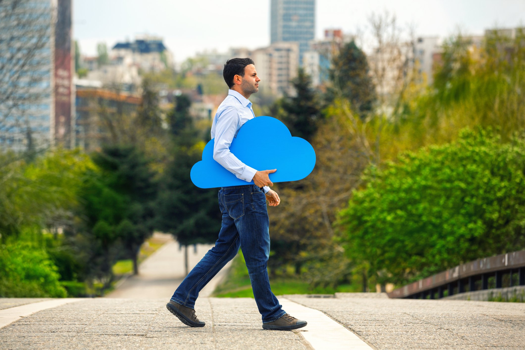 Man walks through a courtyard with a blue cutout of a cloud under his arm. 