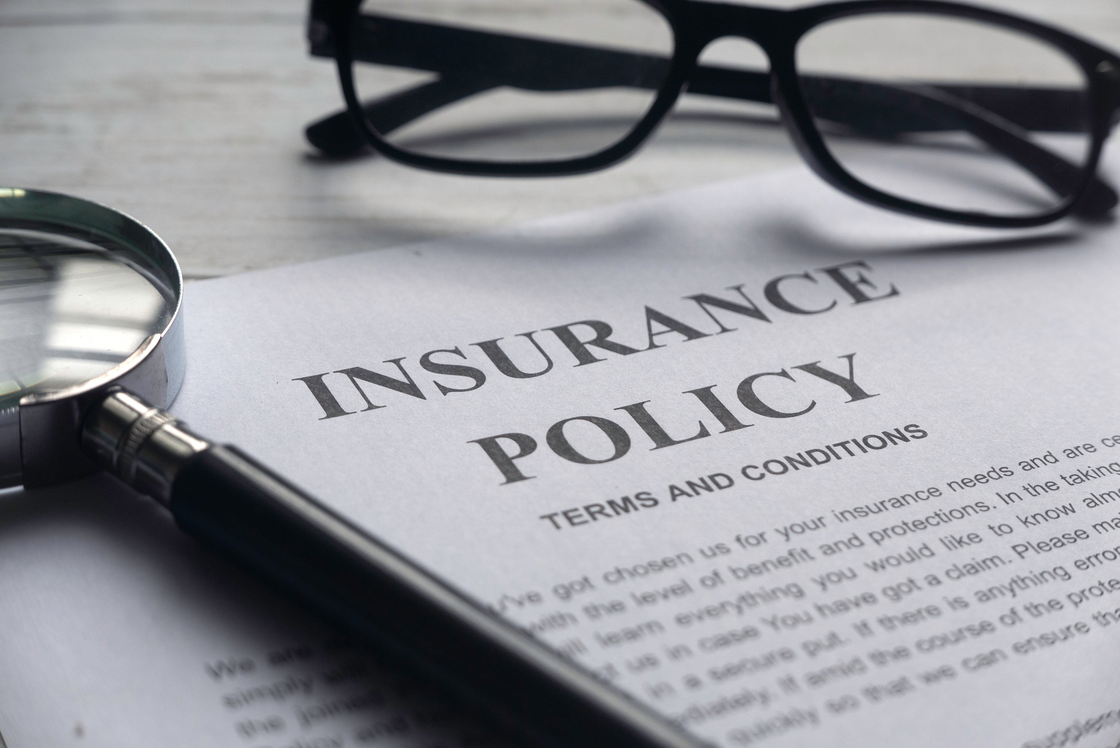 An insurance policy with eyeglasses and a magnifying glass.