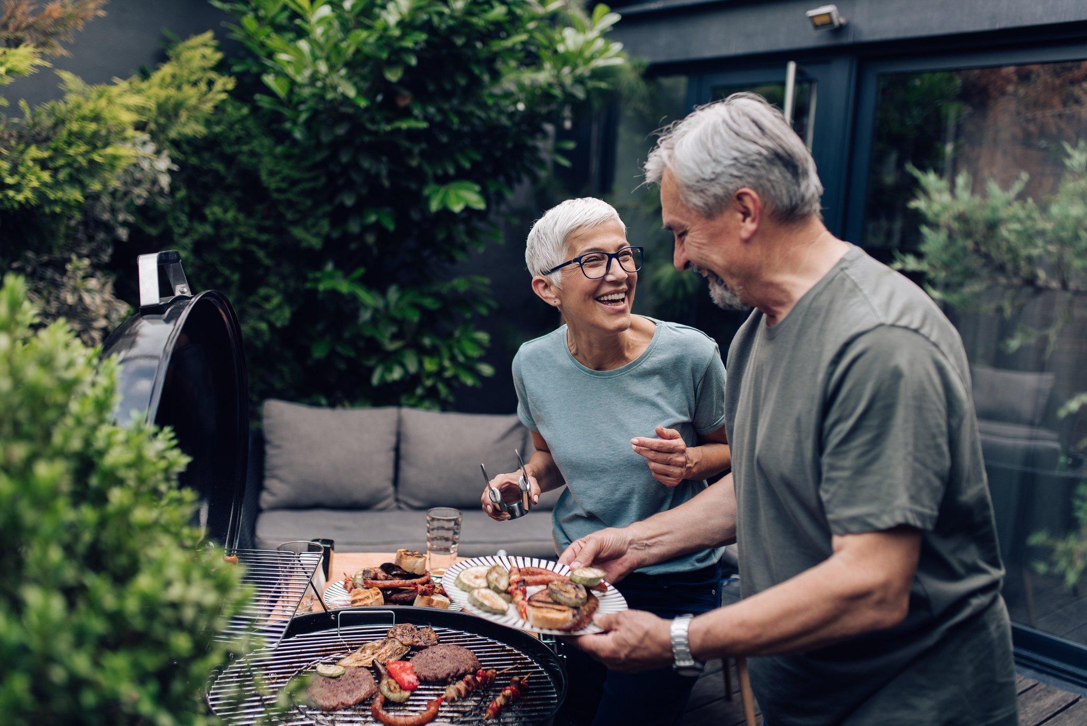 An older couple preparing food on a barbeque. 