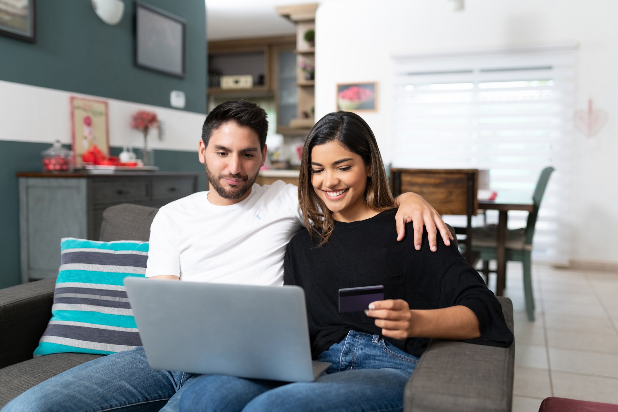 A couple sits on the couch with their computer, making an online purchase.