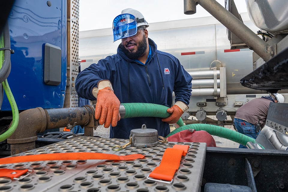 Worker transferring gas from one truck to another.