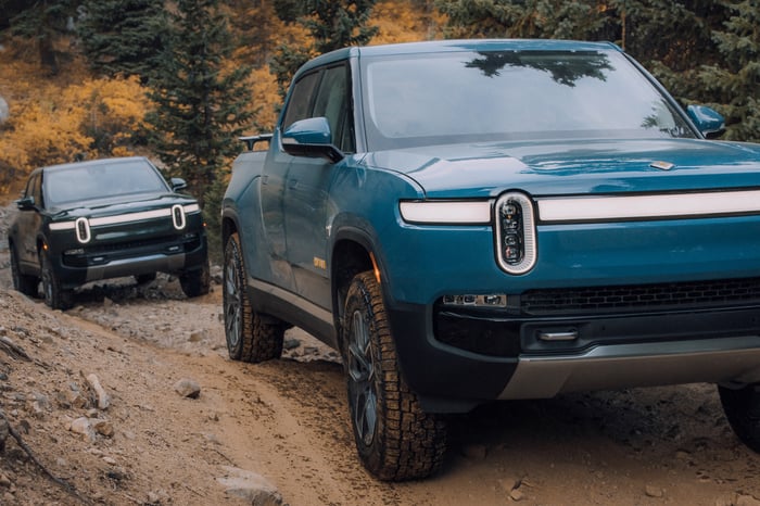 Two Rivian R1T EV pickups climbing a muddy mountainous road.