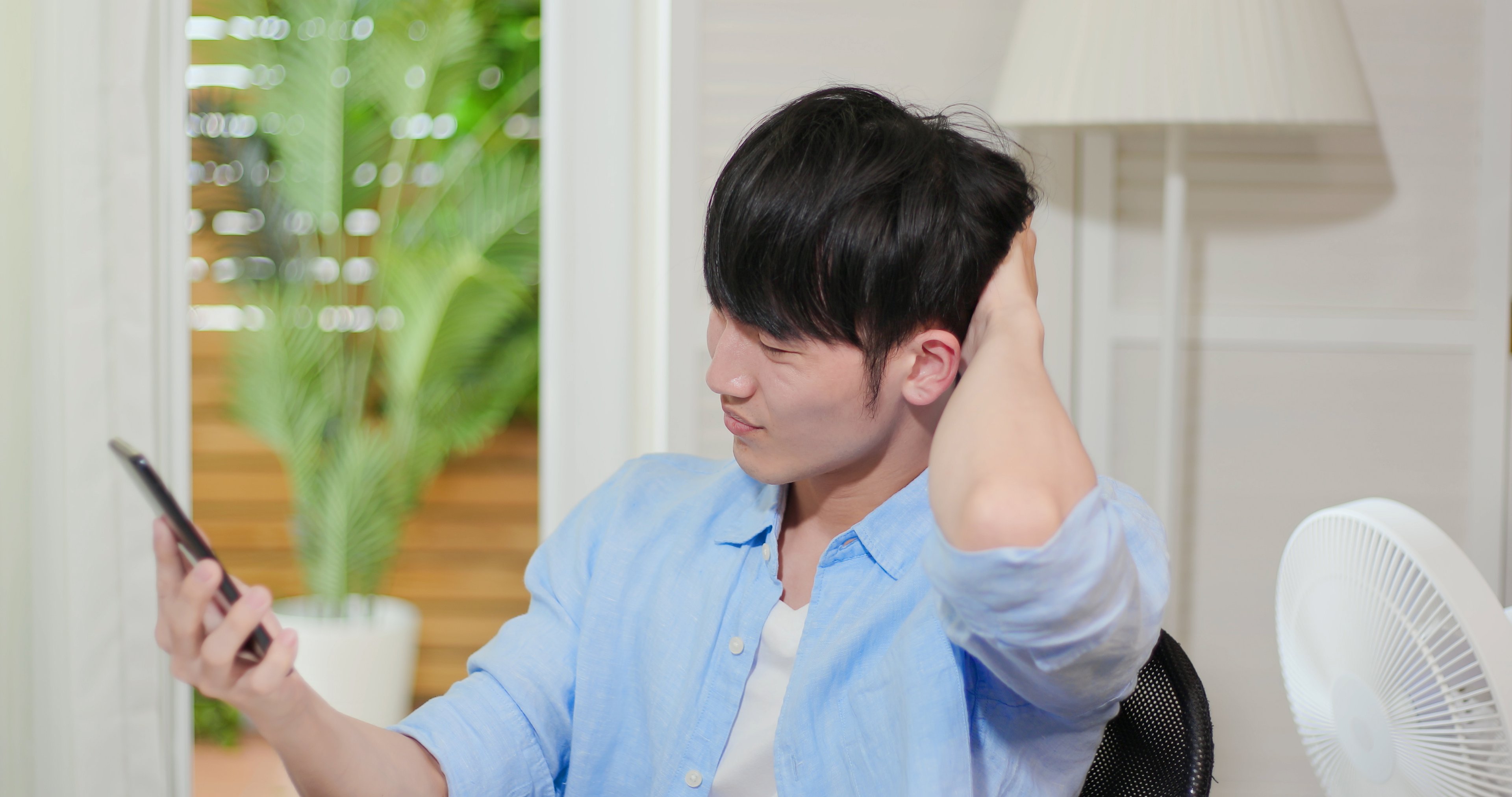 Young man scratches his head looking at his phone. 