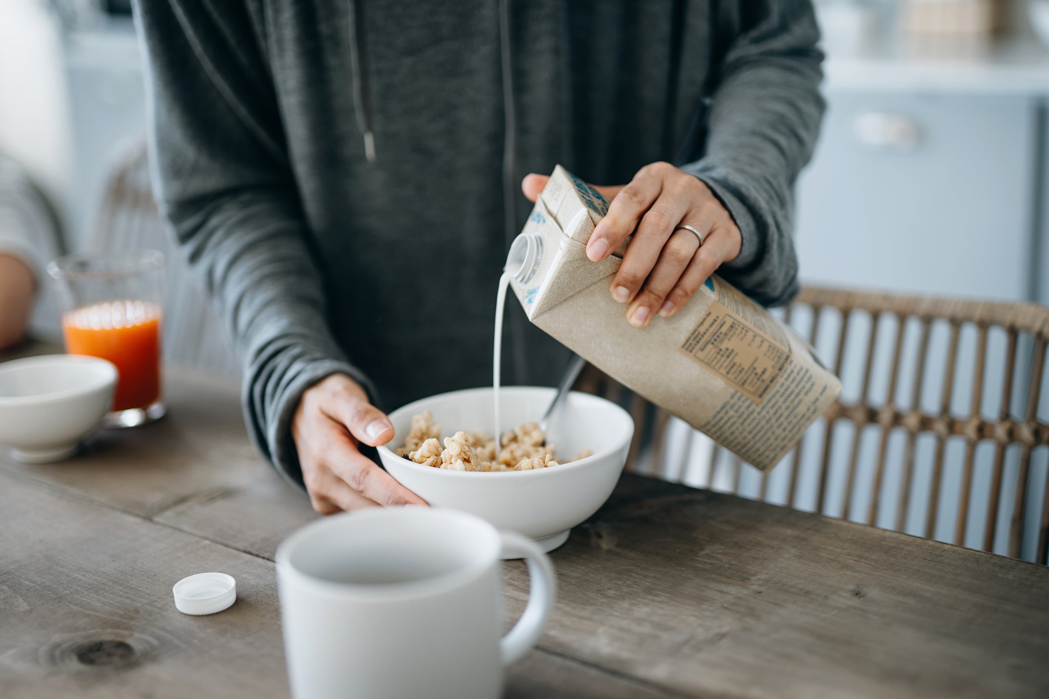 Someone pouring milk over cereal on a kitchen table at home.
