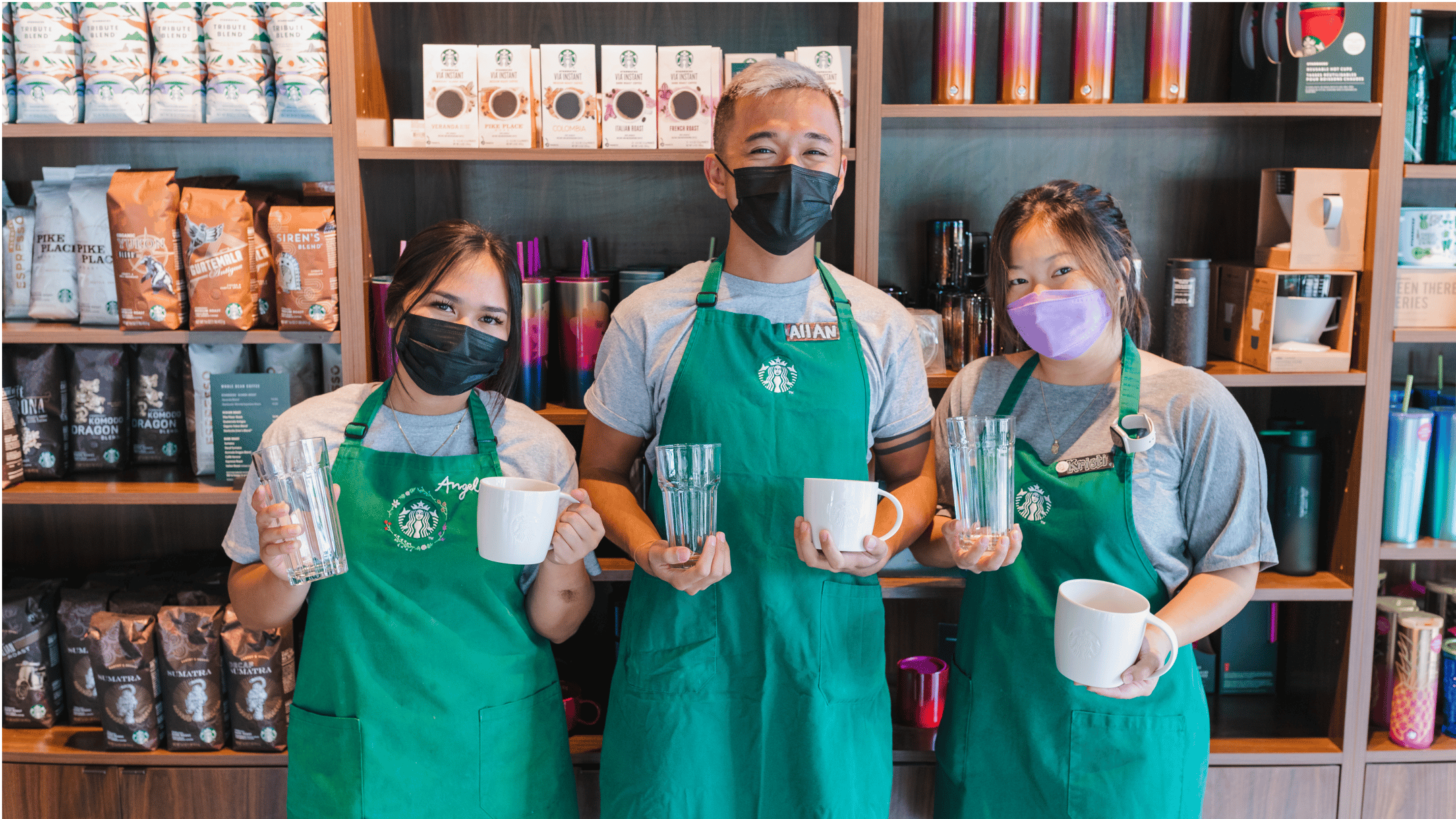 Three Starbucks employees showing off reusable cups.