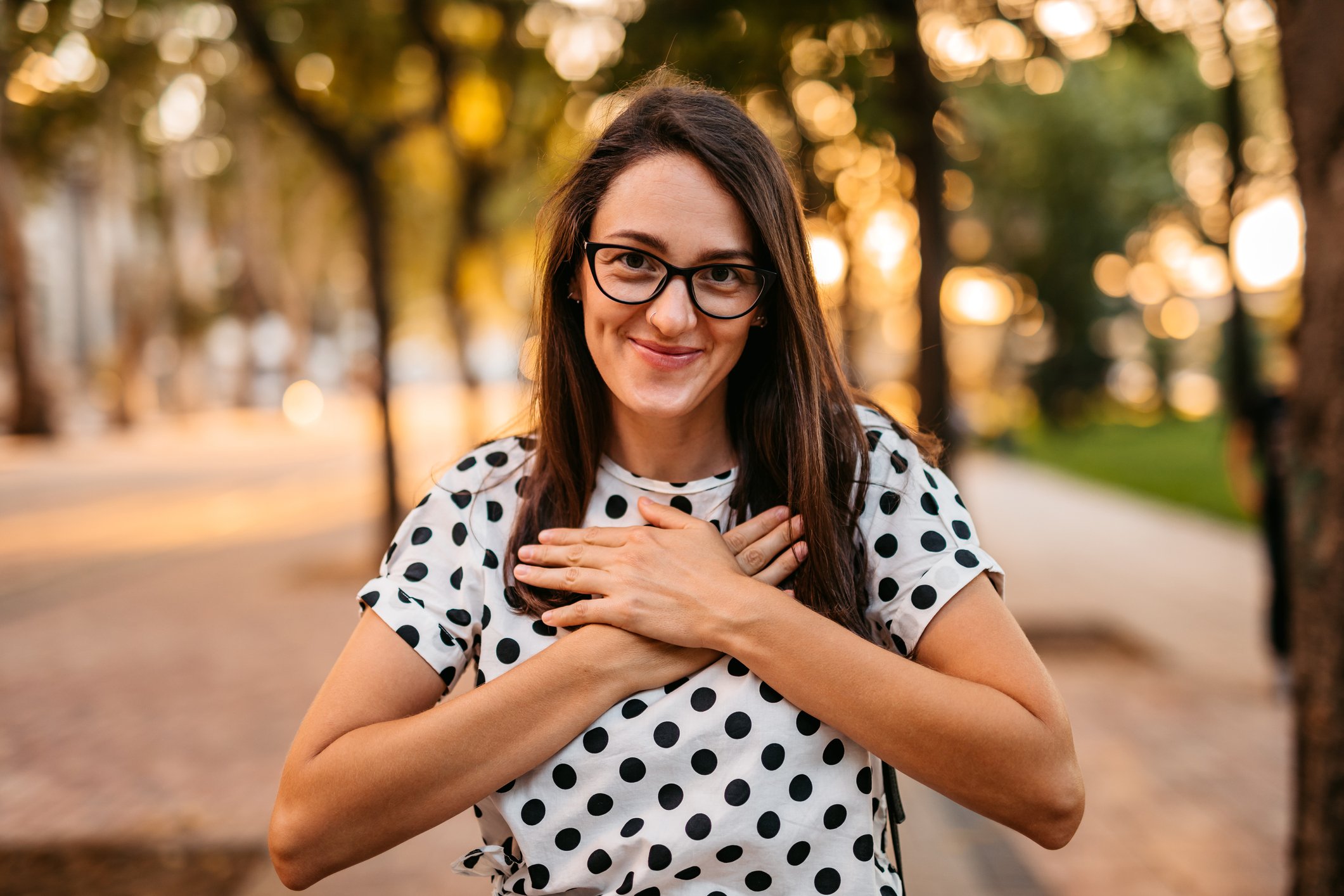 A person is smiling and gesturing using sign language with her hands over her heart.
