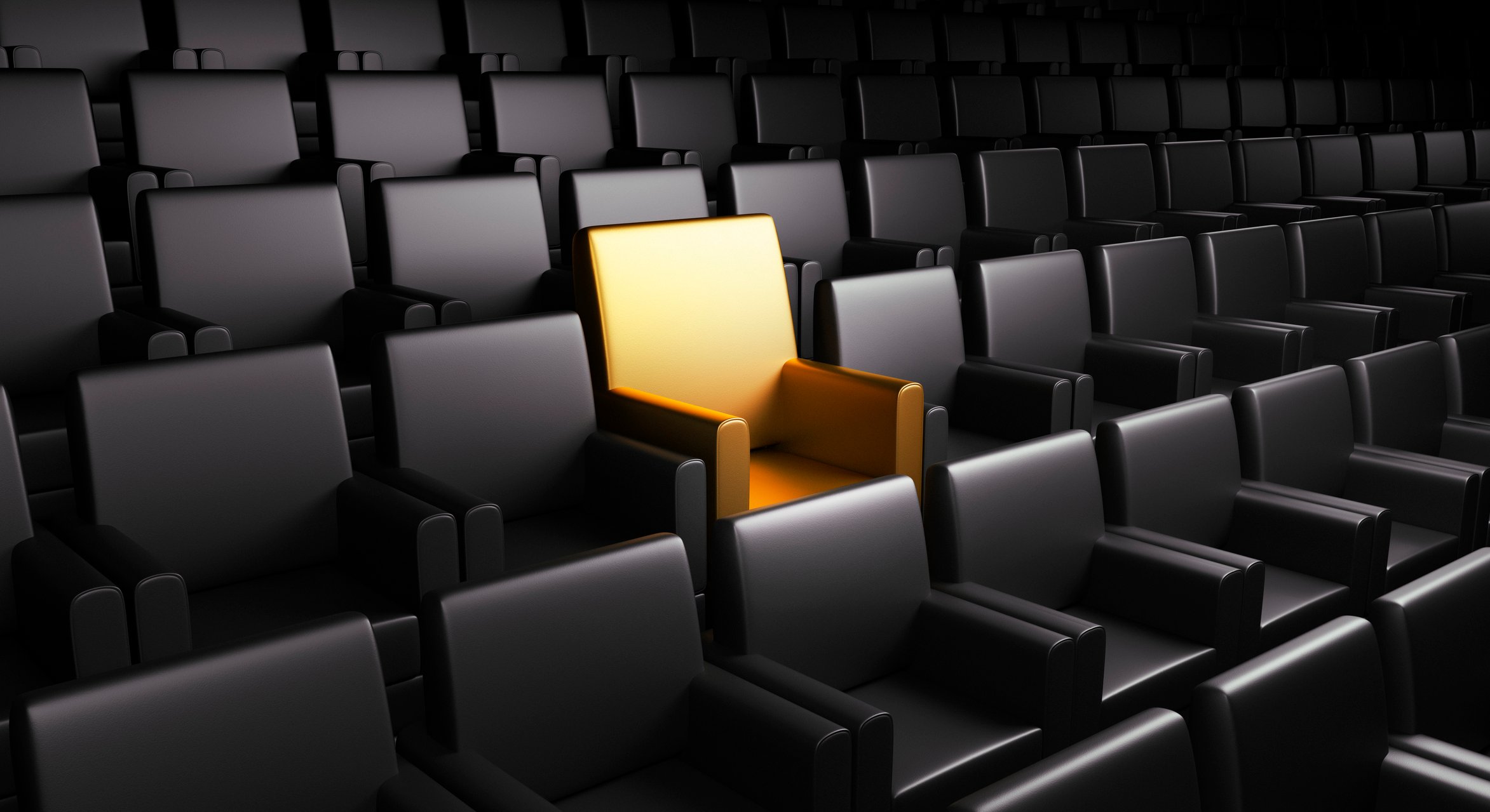 A single golden chair in a theater full of black leather chairs.