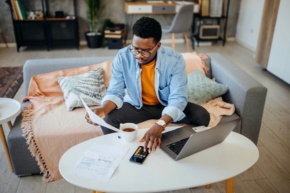 Person calculating taxes on a laptop sitting on a coffee table.
