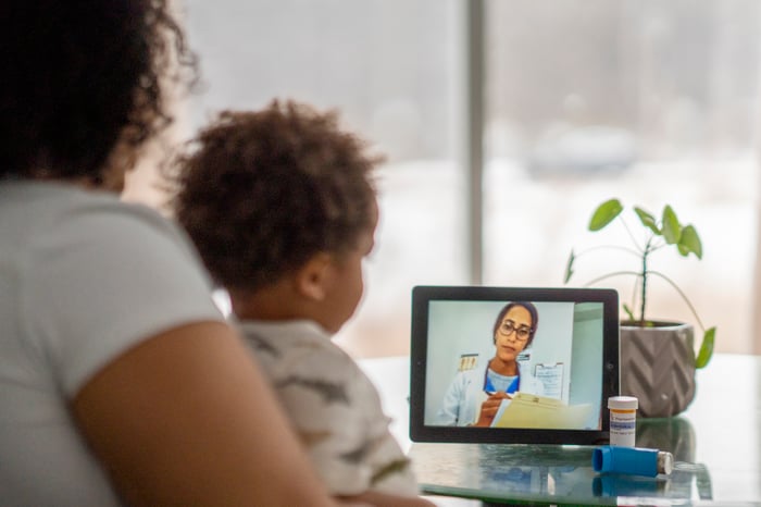 An adult with a child looking at a touchscreen tablet showing a healthcare professional.