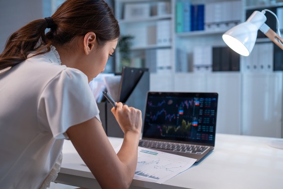 A person looking at a laptop PC displaying stock charts.