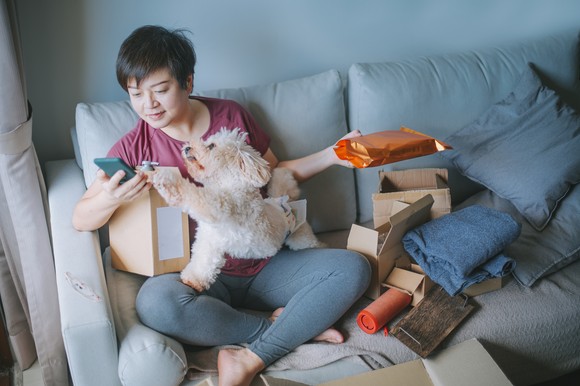 Person sitting on a couch and opening packages, with a dog on their lap.