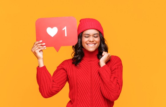Person in red sweater holding up a love button and smiling.