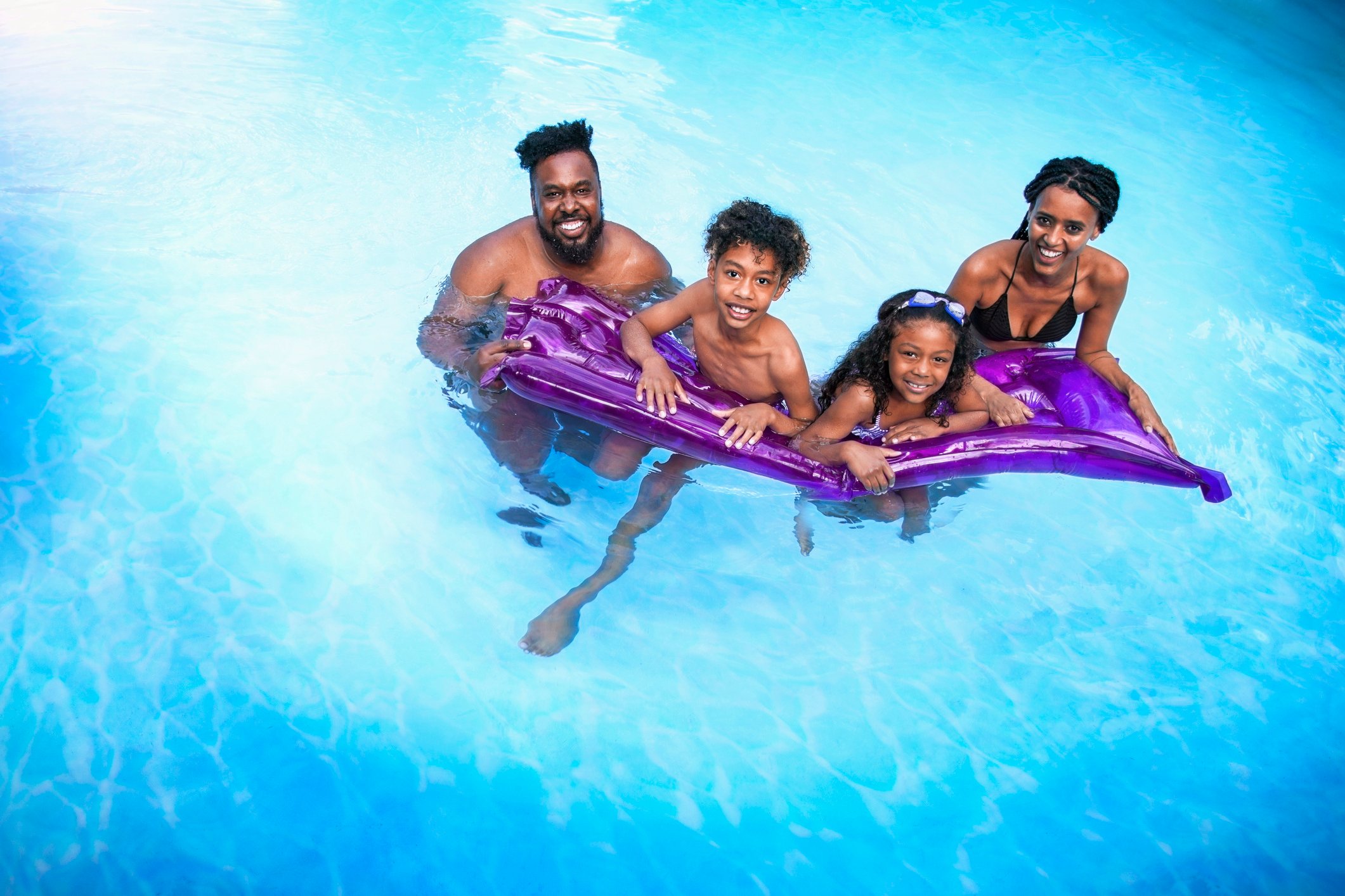 A family of four gathered around a purple float in a pool.