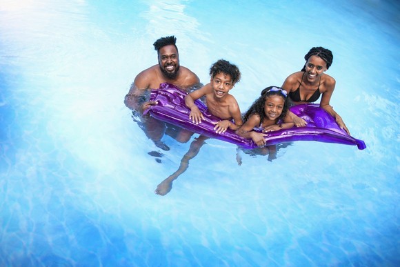 A family of four gathered around a purple float in a pool.