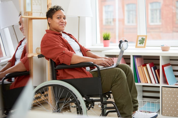 Smiling person in wheelchair with laptop.