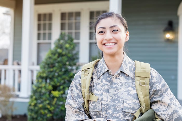 A uniformed soldier standing in front of a house and smiling. 