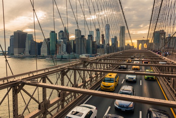 Taxi cabs and other vehicles on Brooklyn Bridge, with New York City skyline behind.