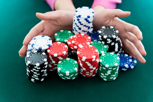 Hands push stacks of white, green, blue, red, and black poker chips forward.