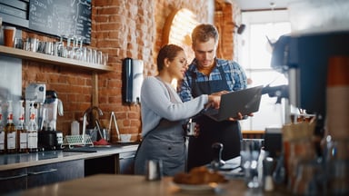 two cafe employees confer over laptop at work