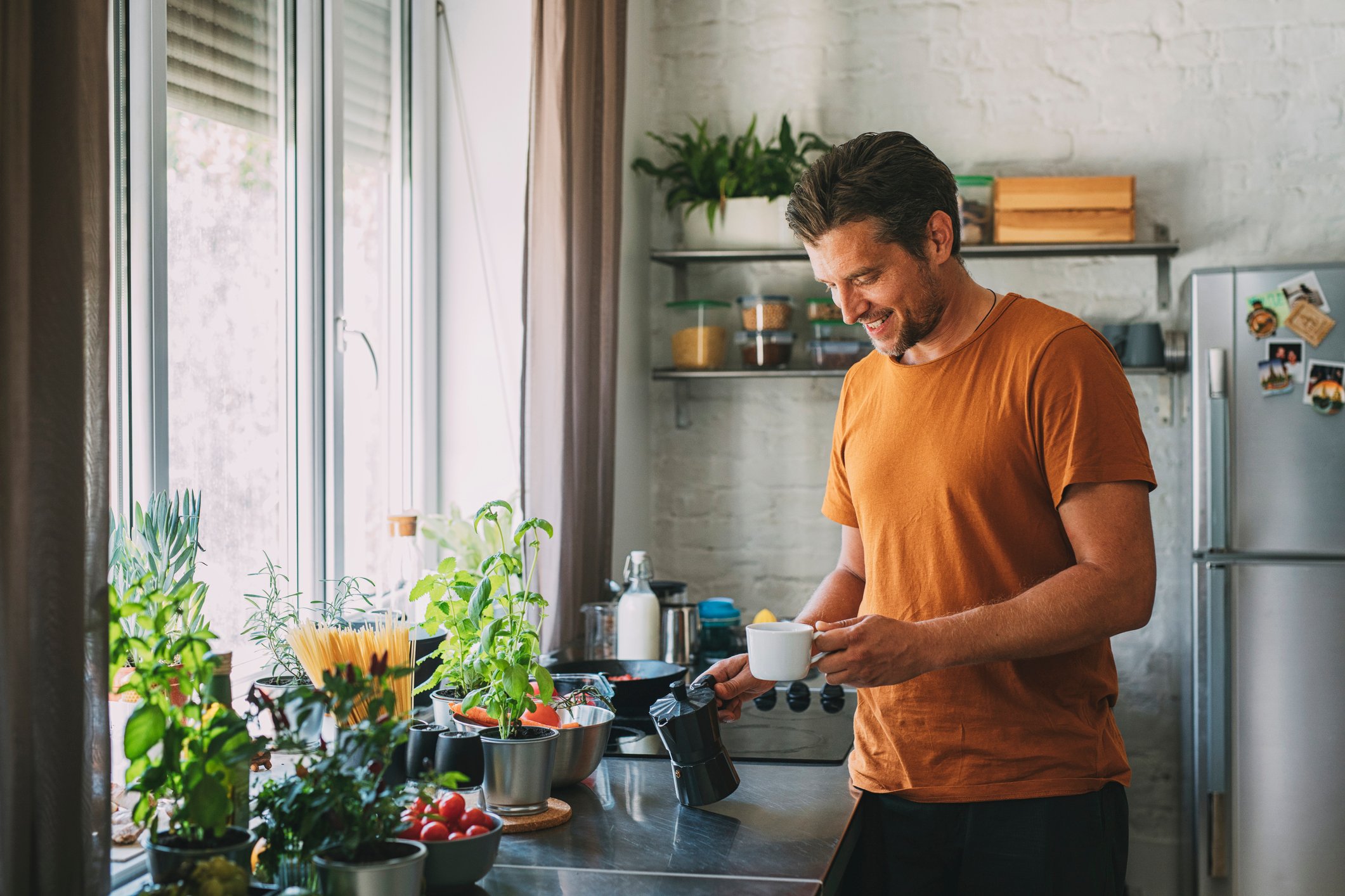 person holding coffee maker and mug in kitchen