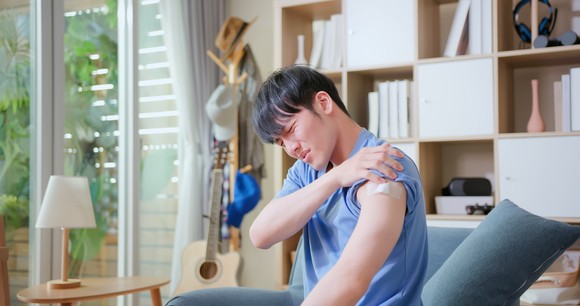 A person grimacing and holding arm with a bandage on the arm.