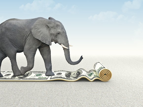 An elephant walking on a roll of $100 bills.