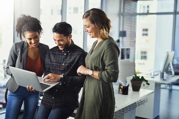 Three people smiling while looking at a laptop.