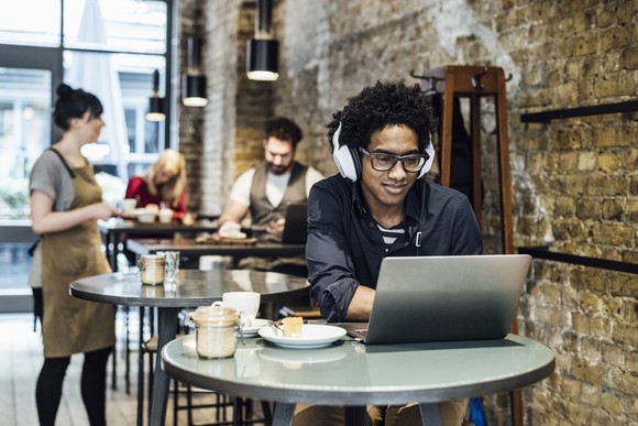 Person wearing headphones working on laptop at cafe.