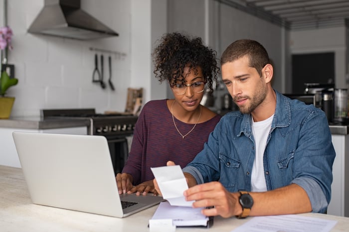 Two people at kitchen table looking at laptop.