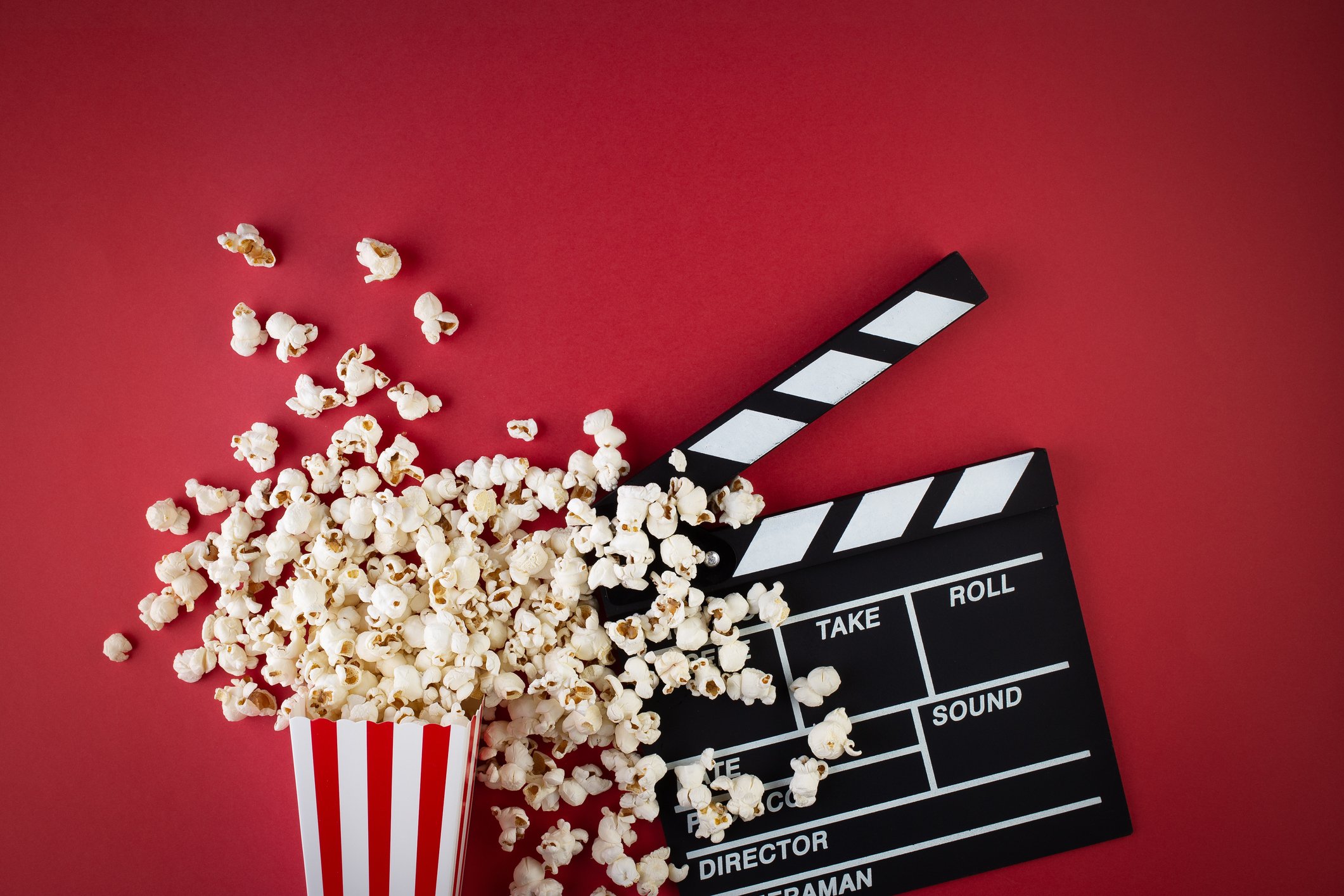 An overflowing box of popped popcorn and a filming slate against a red backdrop.