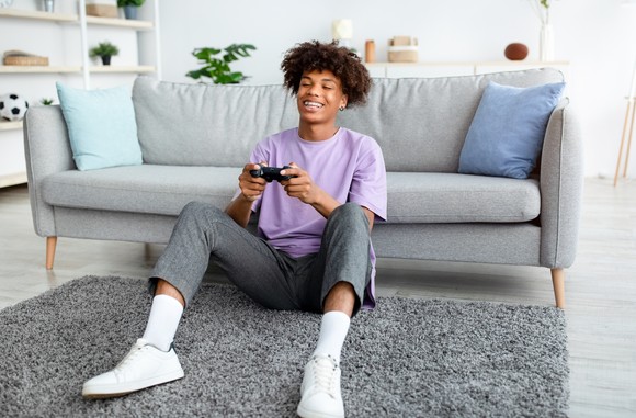 Person sitting on the floor and smiling while playing a console video game.