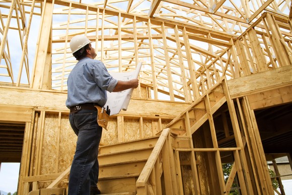 Homebuilder looking at plans in front of partially constructed home.