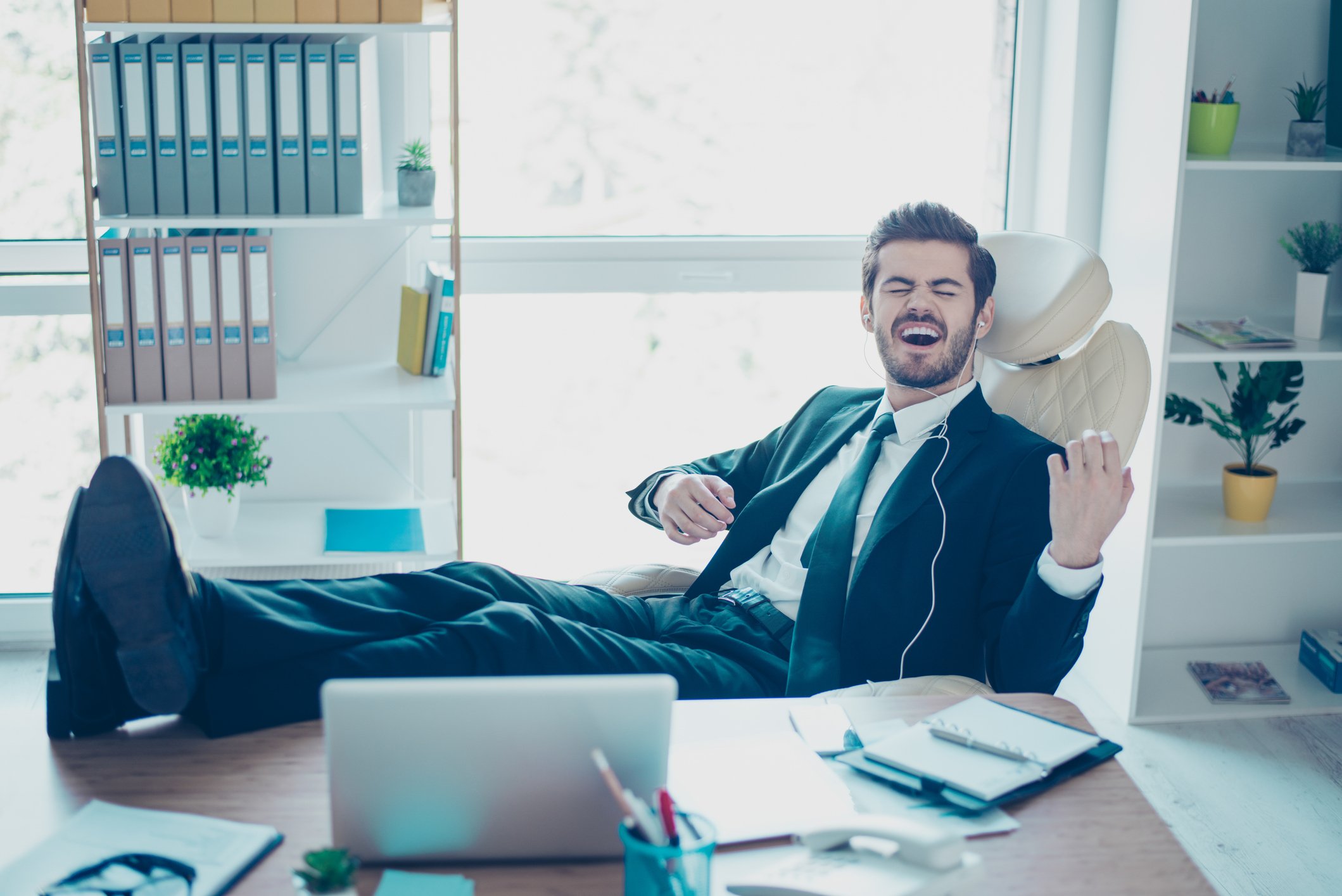 A suited man plays air guitar in his office, as he is clearly happy about something.