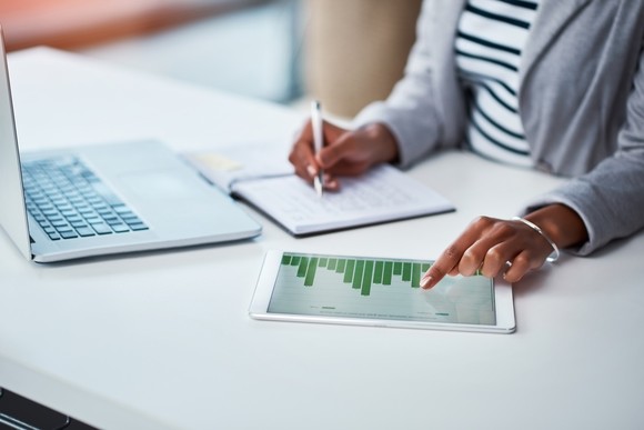 Person analyzing investment charts on a computer, tablet, and notebook.