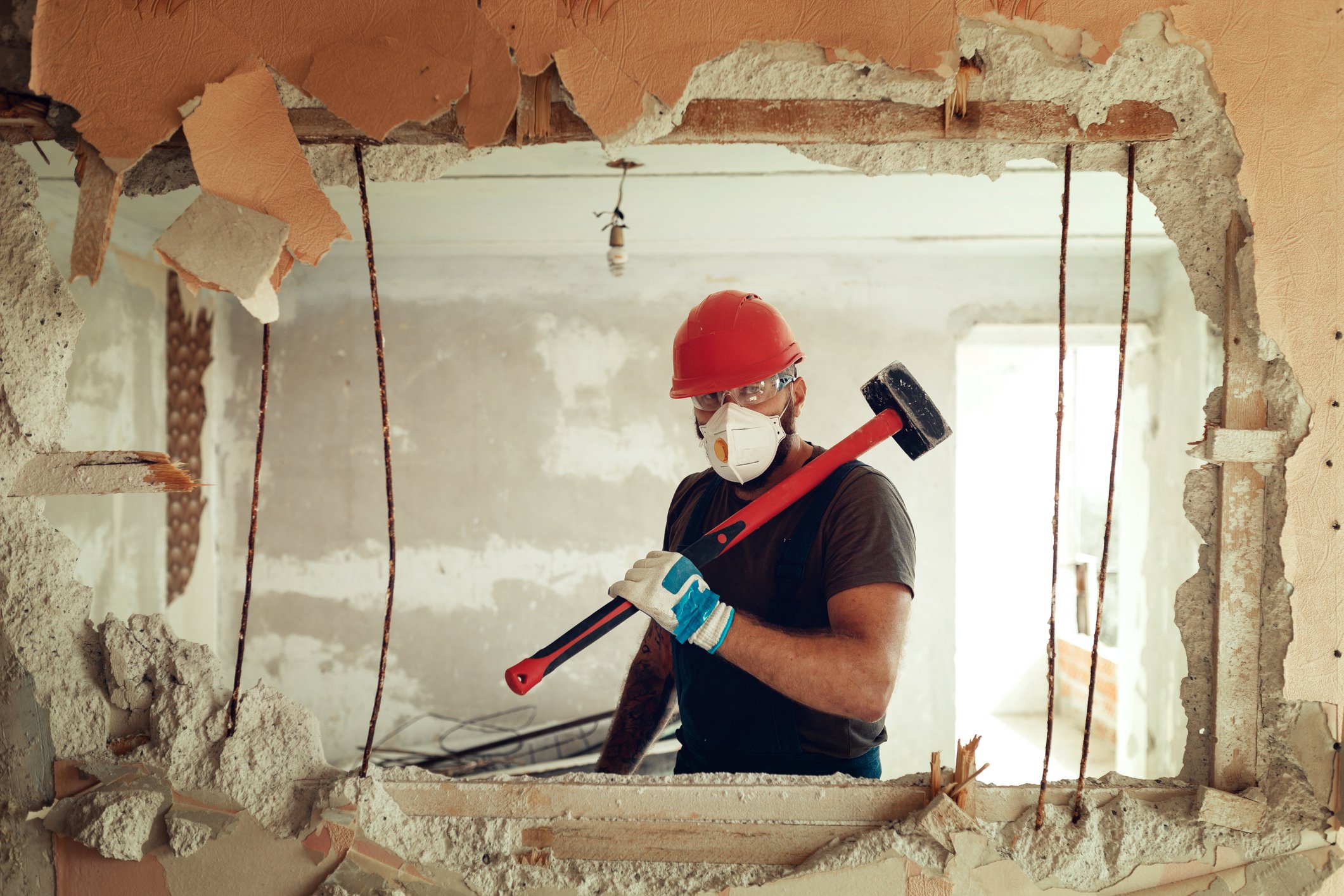 Person holding sledgehammer with construction hat and mask in home.